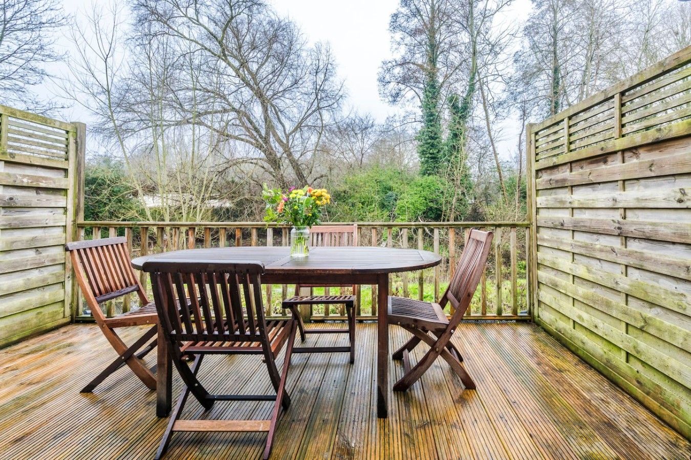 Une terrasse en bois avec une table ronde et quatre chaises, entourée d’une clôture en bois.