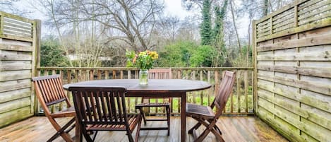 Une terrasse en bois avec une table ronde et quatre chaises, entourée d’une clôture en bois.