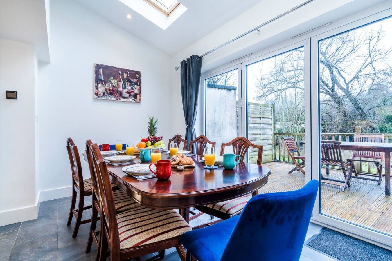 A dining area with a large table set for breakfast, including plates, cups, and a fruit bowl.