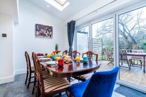 Un coin repas avec une grande table mise pour le petit-déjeuner, comprenant des assiettes, des tasses et un panier de fruits.