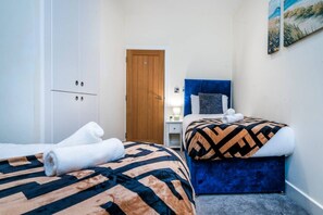A hotel room with two beds, a wardrobe, a door, a nightstand, and a painting on the wall.