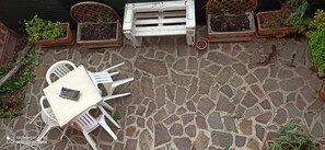 A stone patio with a white table and chairs, surrounded by potted plants and wooden planters. - COZY TOURIST ACCOMMODATION THE REFUGE IN FIUMICINO (Fiumicino)