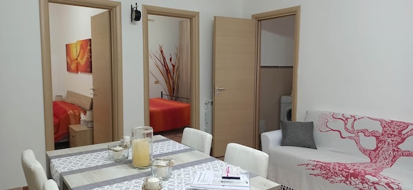 A compact living space with a dining area, a sofa, and a bed with a tree design. - COZY TOURIST ACCOMMODATION THE REFUGE IN FIUMICINO (Fiumicino)