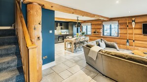 A modern interior with a wooden staircase, a living area with a sofa, a dining table, and a kitchen in the background. - The Lookout (Ilkley)