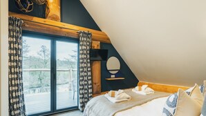 A bedroom with a large window, a bed with pillows, a wooden ceiling, and a TV on the wall. - The Lookout (Ilkley)