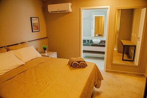 Habitación de hotel con cama, una mesita de noche con planta, baño visible a través de una puerta abierta y un espejo con cortina amarilla.