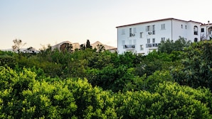 A white multi-story building with balconies, surrounded by dense greenery and mountains in the background. - Bright Accommodation in Orosei (Orosei)