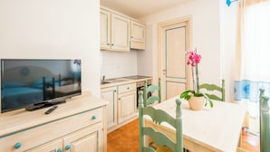 A compact kitchen with white cabinets, a dining table, and a TV. - Bright Accommodation in Orosei (Orosei)