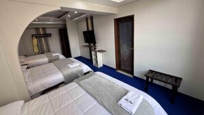 Habitación de hotel con tres camas, un banco, un televisor y una puerta con un cartel.