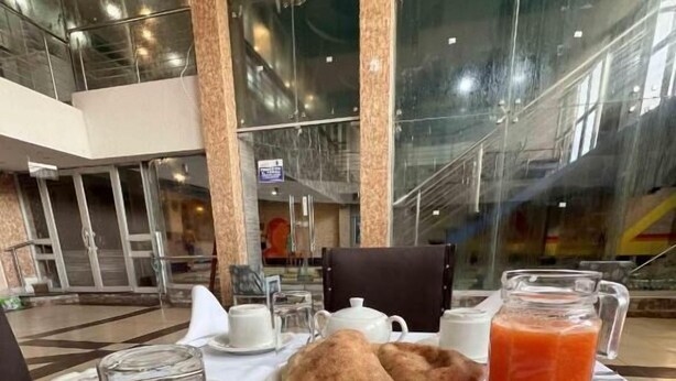 Una mesa de desayuno con un plato de pasteles, una jarra de jugo de naranja, una taza de café y un recipiente pequeño de mantequilla.