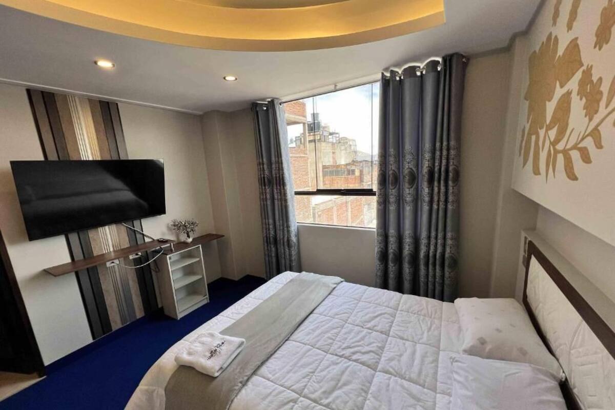 Habitación de hotel con cama, un televisor de pantalla plana montado en la pared, ventana con cortinas y vistas de la ciudad.