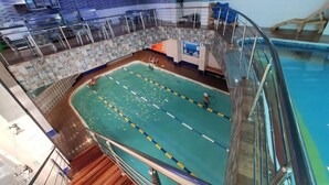 Una piscina interior con carriles de natación, un trampolín y una zona de cubierta de madera.