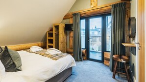A bedroom with a bed, a wooden chair, a TV, and a sliding glass door leading to an outdoor area. - Keepers Cabin (Ilkley)
