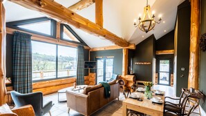 A spacious living area with a large window, wooden beams, a sofa, a dining table set for four, and a television. - Bears Den (Ilkley)
