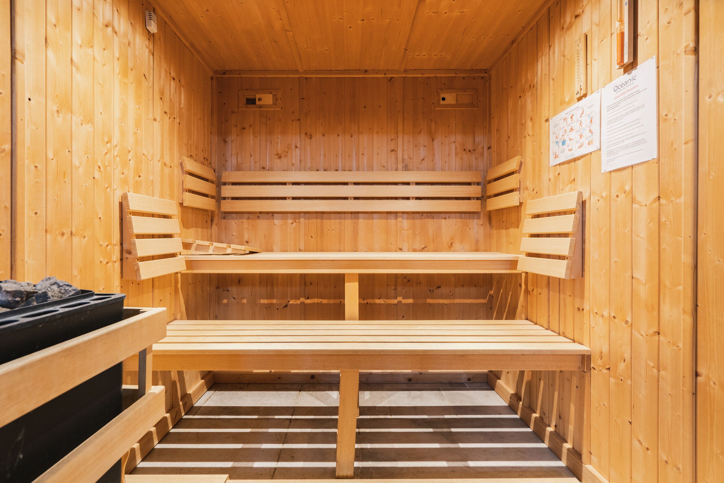 A sauna with wooden benches and a bench with a black container on the left.
