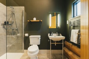 A modern bathroom with a glass-enclosed shower, a toilet, a sink, and a wooden bench. - Bears Den (Ilkley)