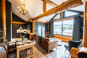 A cozy cabin interior with a dining area, sofa, and large windows offering a view of the outdoors. - Bears Den (Ilkley)