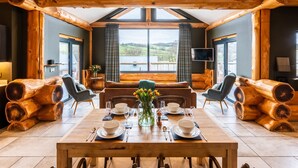 A dining area with a wooden table set for four, surrounded by chairs, with a view of the countryside through large windows. - Bears Den (Ilkley)