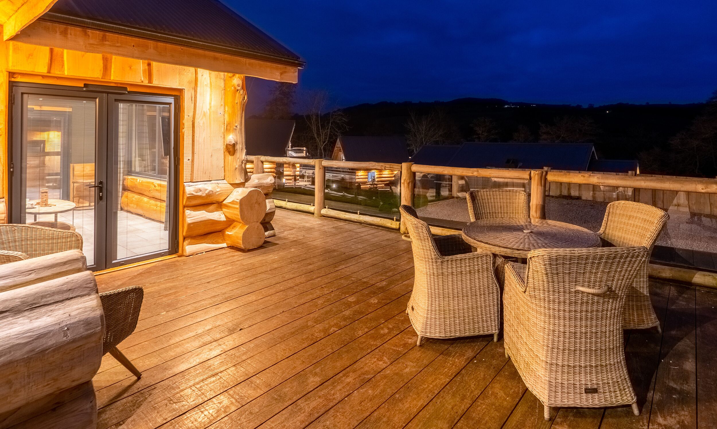 En træterrasse med fletmøbler og en glasdør, der fører til et indre rum.