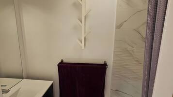 Un baño con un lavamanos blanco, un perchero con una toalla oscura y una ducha con pared de azulejos estampados.