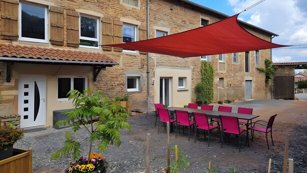 Un edificio in pietra con patio, posti a sedere all'aperto e un telo ombreggiante rosso.