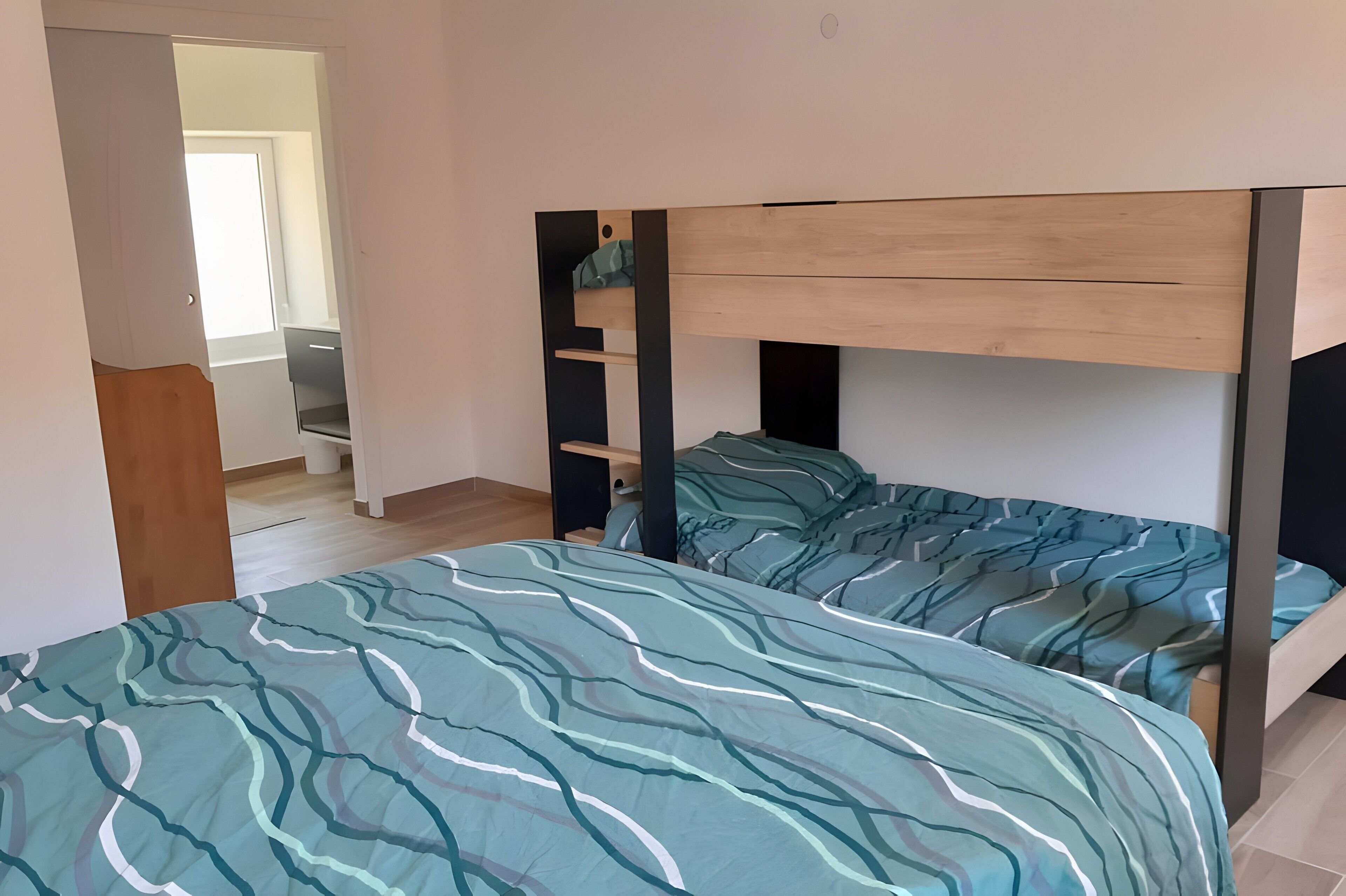 A bedroom with bunk beds, a wooden headboard, and a view of a hallway.