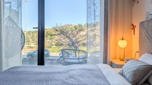 Ein Hotelzimmer mit großem Fenster, einem Bett, einem Sessel und einem Nachttisch mit Lampe.
