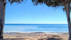Ein Strand mit blauem Himmel, ruhiger See und felsigem Ufer.