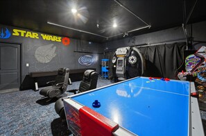 Quarto com mesa de pebolim azul, decoração temática de Star Wars, cadeira gamer e um banquinho azul pequeno.
