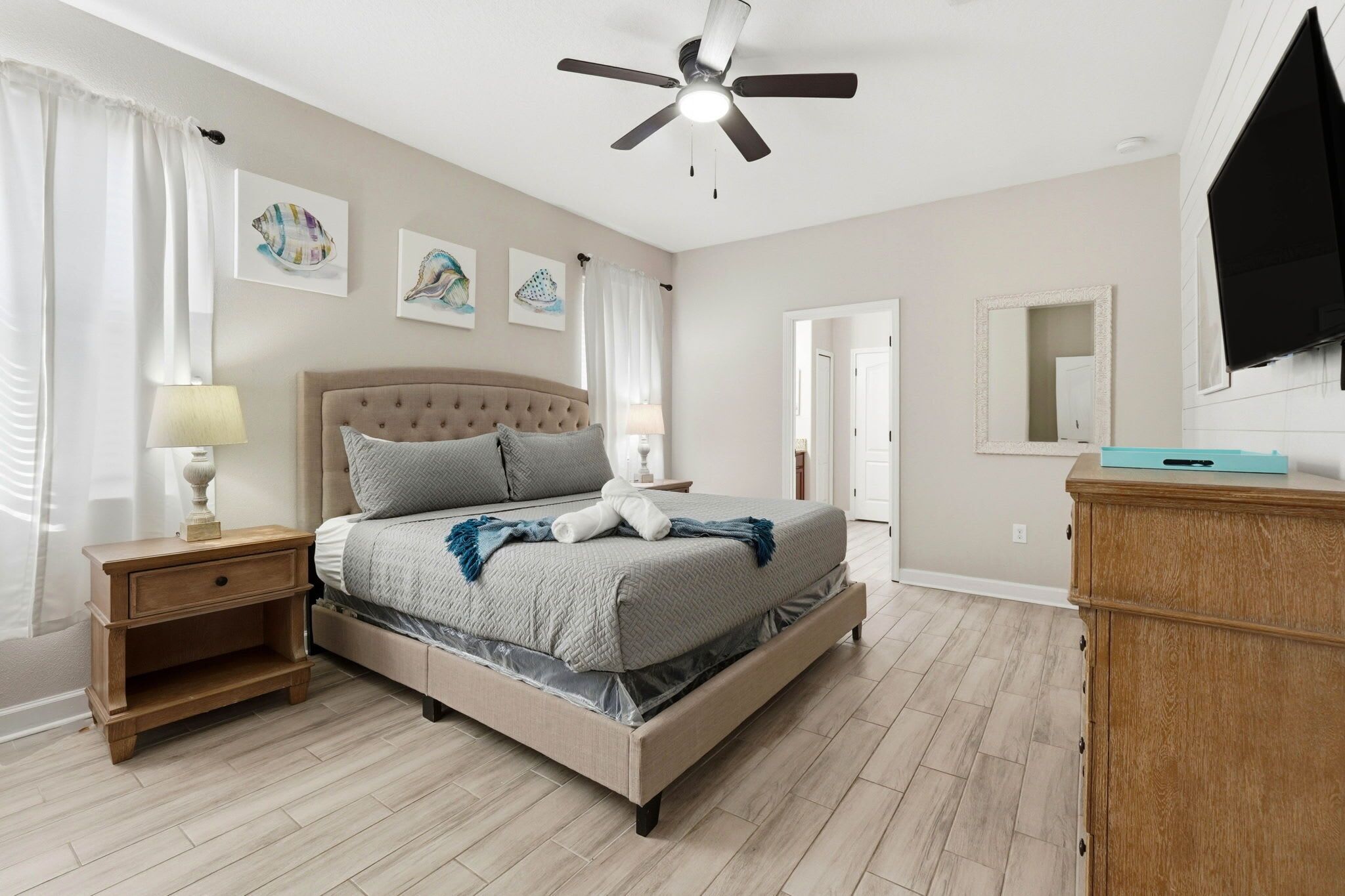 A bedroom with a bed, nightstand, ceiling fan, artwork on the wall, and a television.