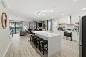 Une cuisine moderne dotée d’un grand îlot central, de tabourets de bar, d’un four encastré et d’un réfrigérateur.