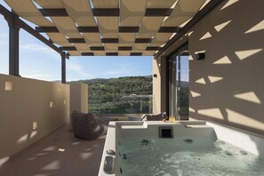 A balcony with a hot tub, a view of the countryside, and a pergola providing shade.