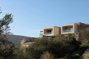 A modern two-story building with balconies, surrounded by vegetation and a clear sky.