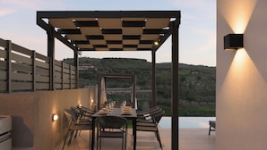 Uma área de refeições ao ar livre com pérgola xadrez, mesa posta para quatro pessoas e vista para uma paisagem montanhosa ao fundo.