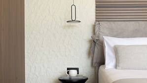Quarto de hotel bem arrumado, com uma cama, mesa de cabeceira com uma xícara e um livro, parede texturizada e luminária pendente.