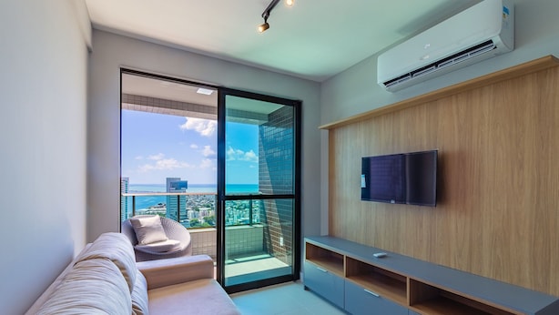Un salon moderne avec un canapé, un téléviseur fixé à un mur en bois et un balcon offrant une vue sur la ville.