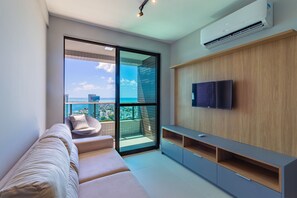 A modern living room with a sofa, a TV mounted on a wooden wall, and a balcony with a city view. - Parque Shopping #2001 - Pina by Carpediem (Recife)
