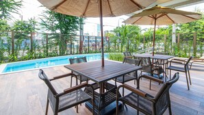 Un espace aménagé au bord de la piscine, avec une table en bois et des chaises en osier, le tout entouré de parasols.