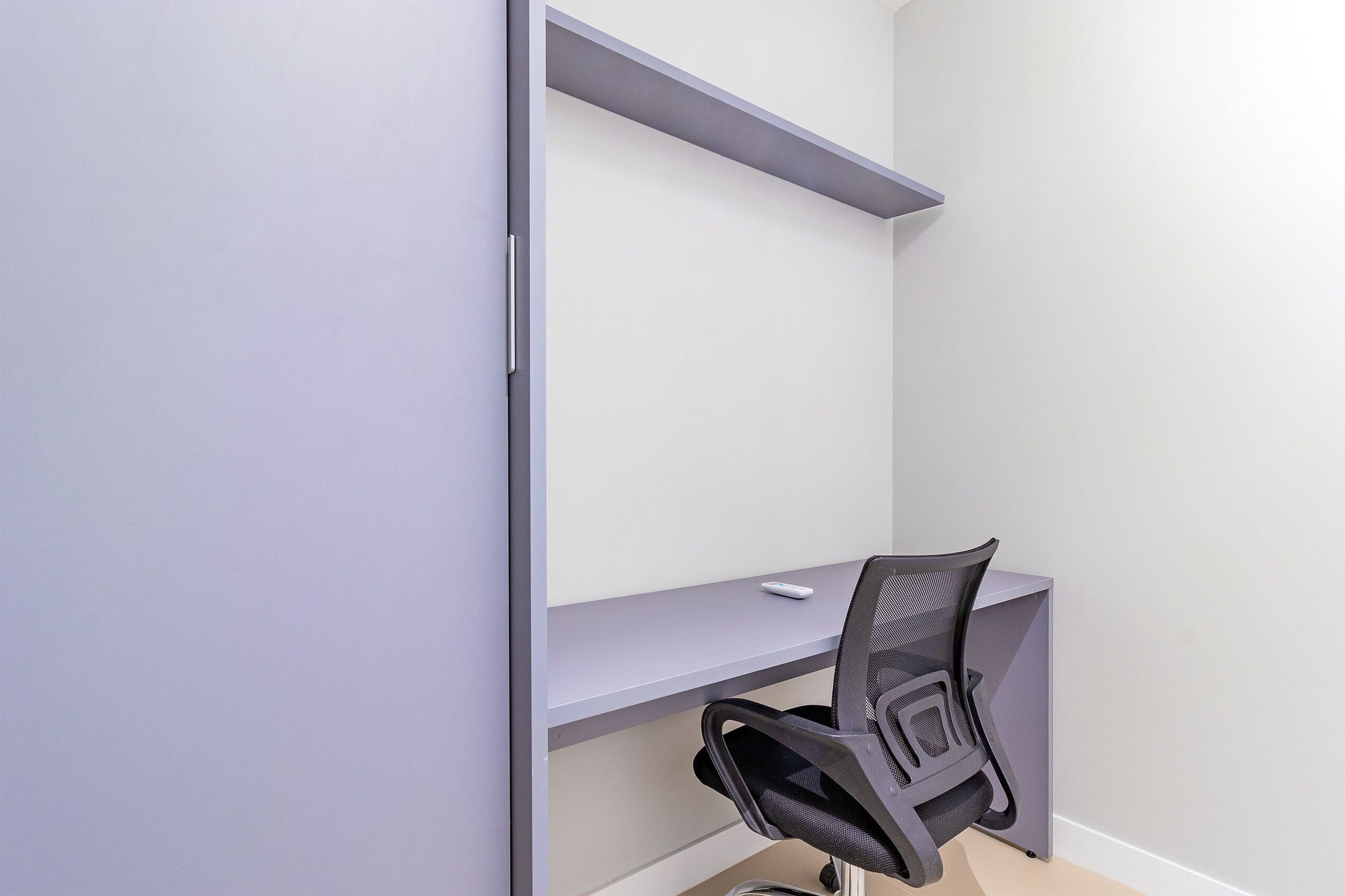 Un espacio de oficina moderno con un escritorio gris, una silla de malla negra y una pared blanca.