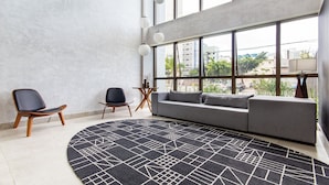Un salon moderne avec une grande fenêtre, un canapé gris, un tapis noir et blanc et deux chaises en bois.