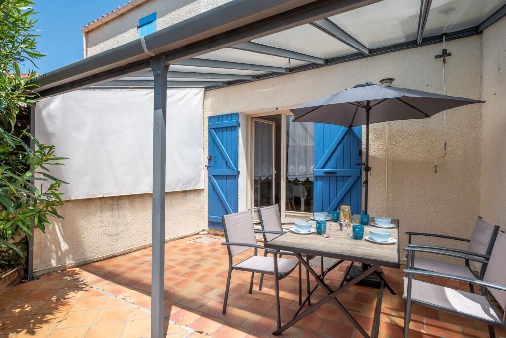 Una veranda riparata con tavolo e sedie, una porta blu e una finestra con persiane blu.