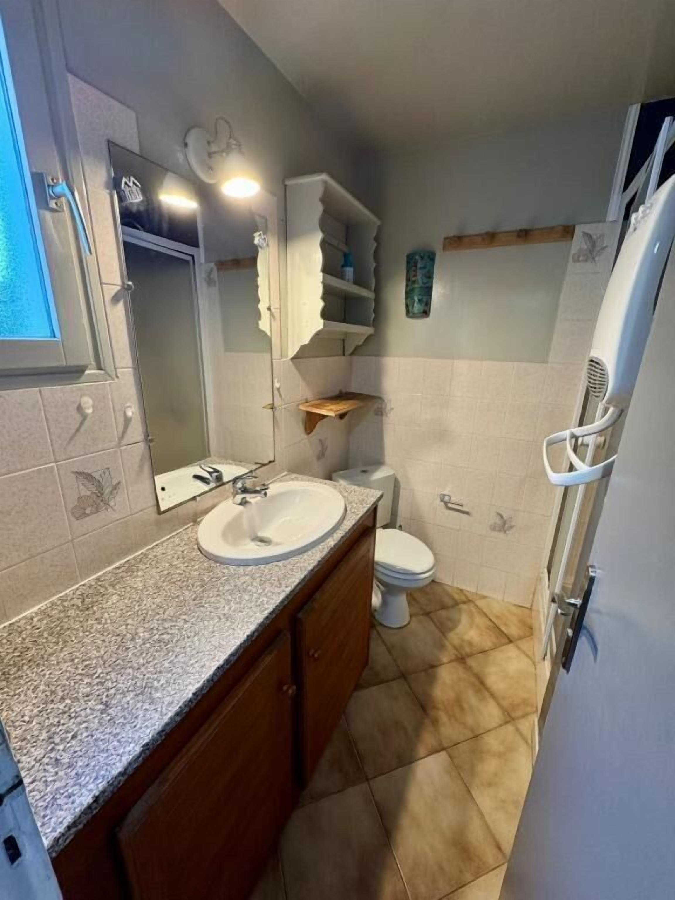 A bathroom with a sink, mirror, toilet, and shower area.