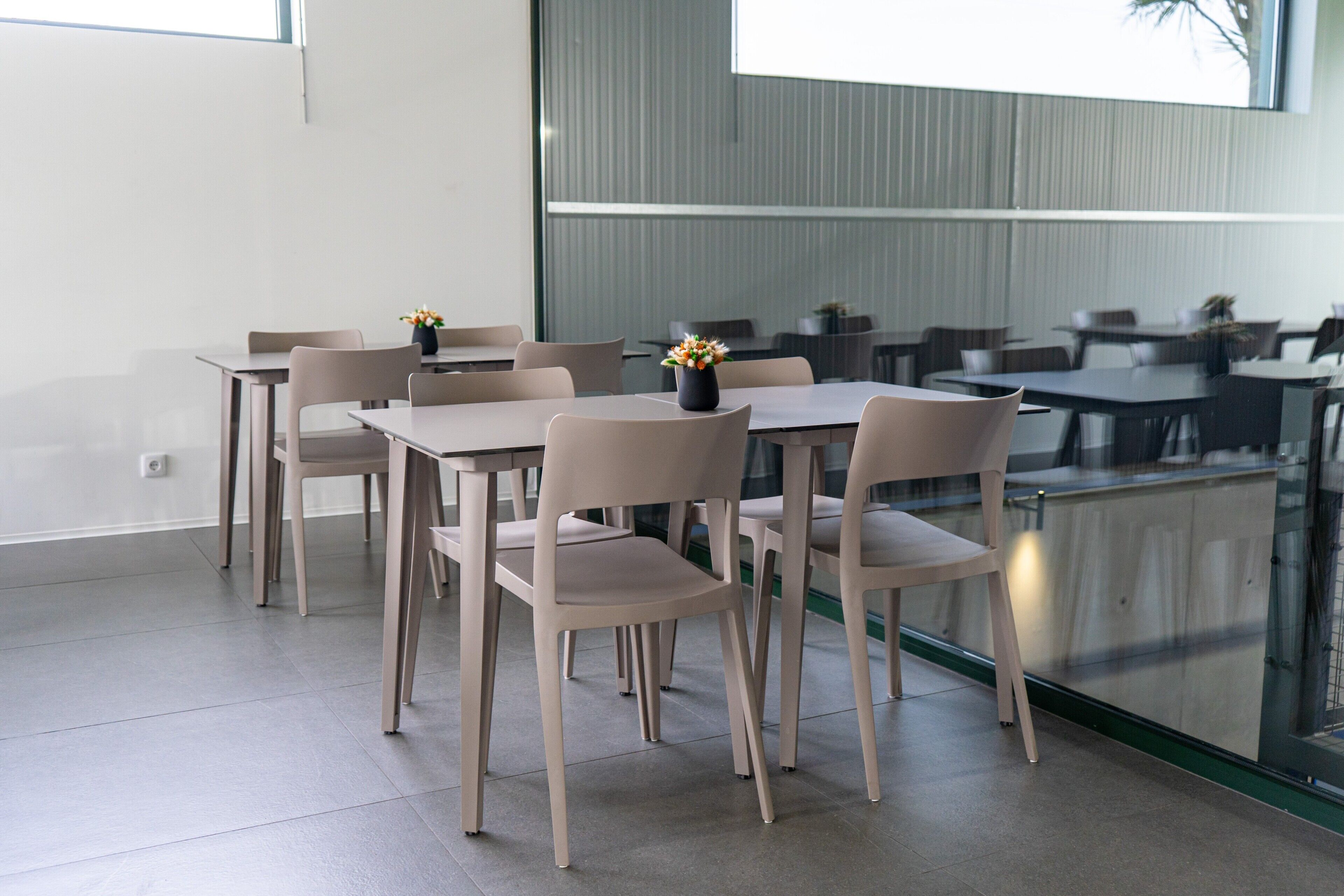 A modern dining area with tables and chairs, a vase with flowers, and a view through a glass wall.