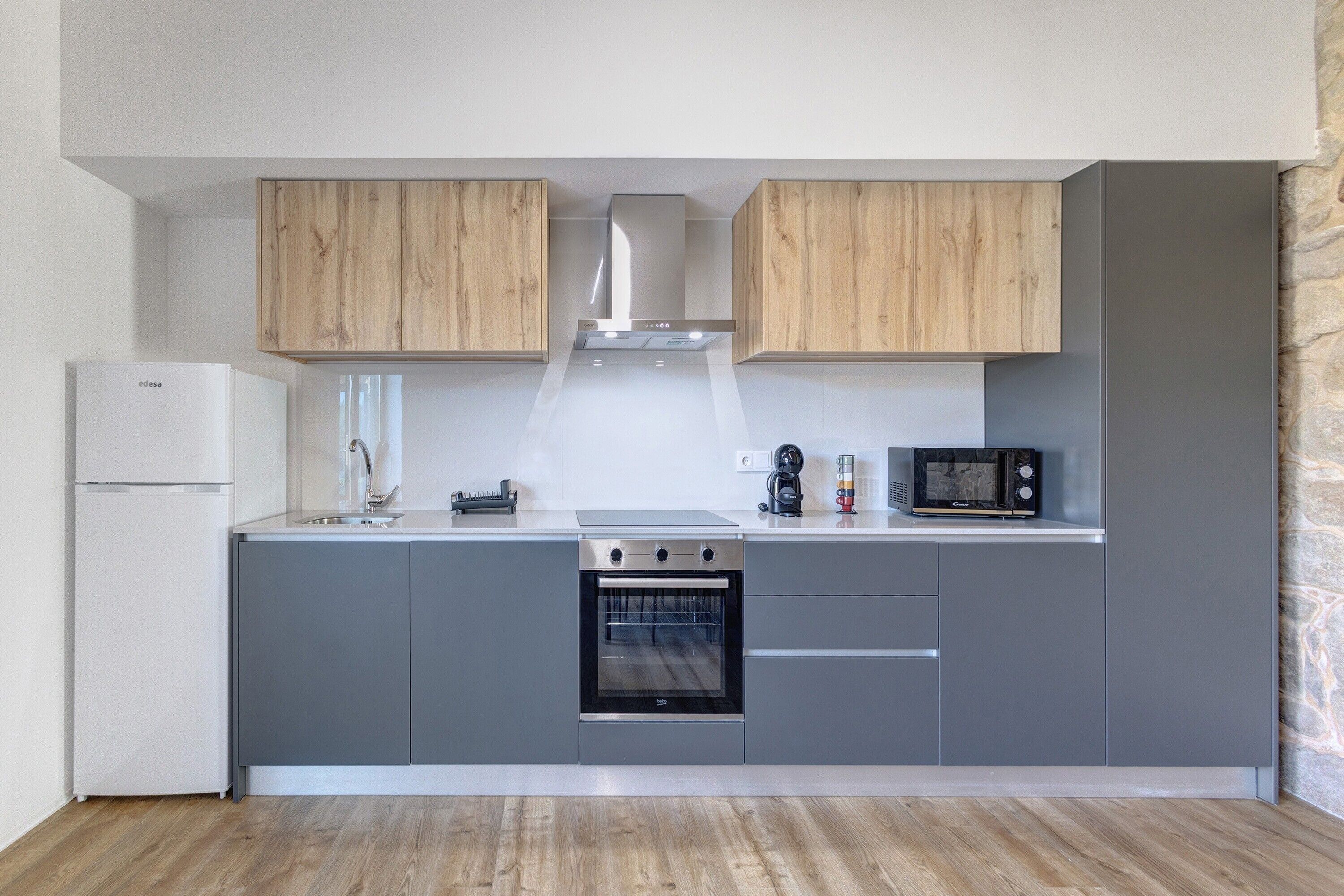 A modern kitchen with grey cabinets, a built-in oven, a microwave, and wooden upper cabinets.