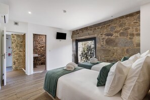 A bedroom with two beds, stone walls, a TV, and a window. - Apartment 'T2 Familiar Ua01' with Shared Pool, Wi-Fi and Air Conditioning (Palmeira)