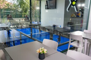 A room with a glass partition, a tennis court, and a table with a vase. - Apartment 'T2 Familiar Ua01' with Shared Pool, Wi-Fi and Air Conditioning (Palmeira)