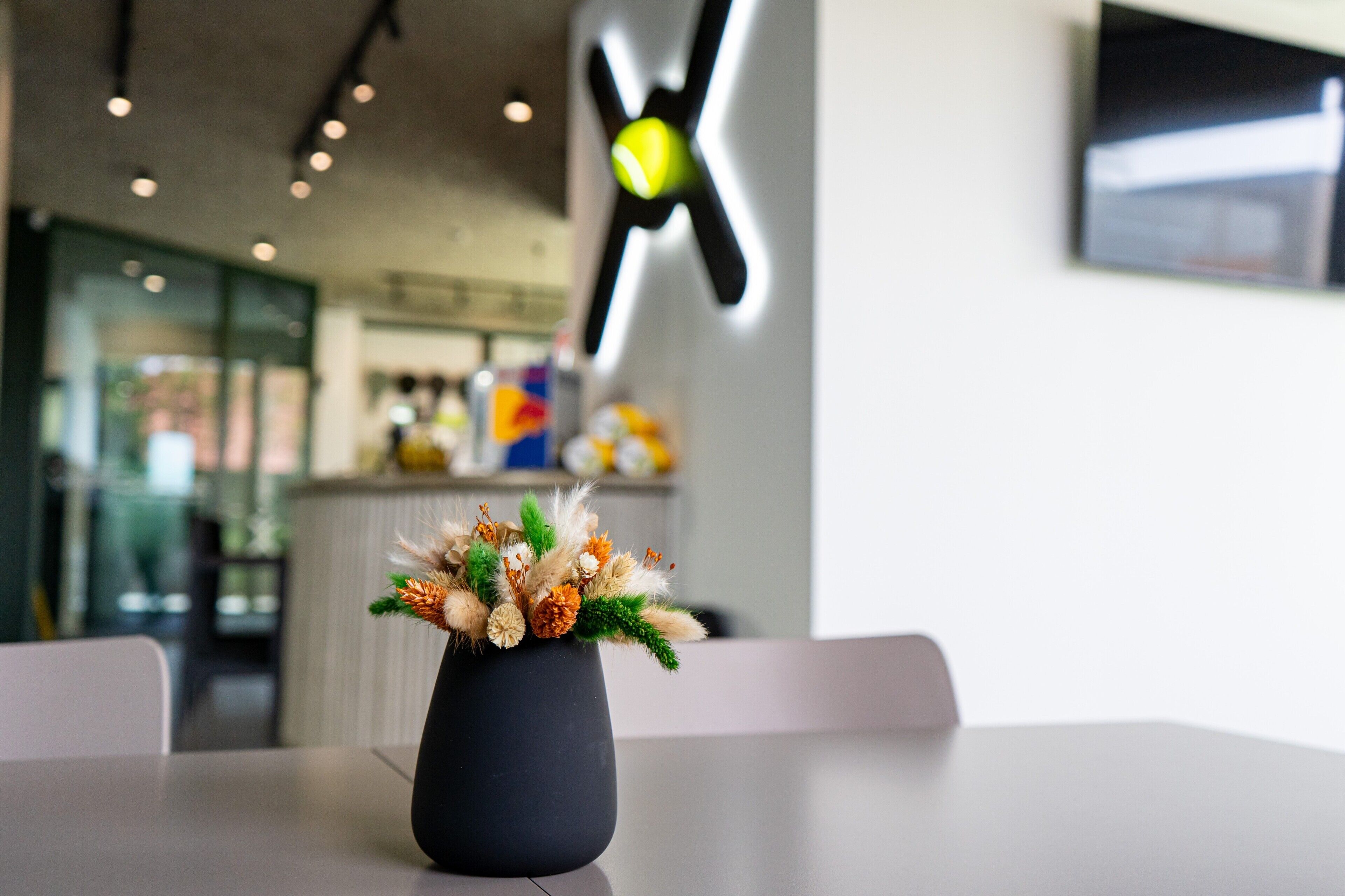 Una mesa con un jarrón de flores secas, un interior moderno con un letrero de neón y una encimera con varios objetos.