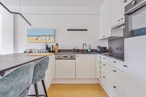 A modern kitchen with white cabinets, a dishwasher, and a countertop with various appliances. - Catamaran 0502 met garage (Nieuwpoort)