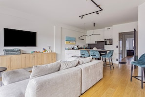 A modern living room with a grey sectional sofa, a wooden cabinet, and a flat-screen TV mounted on the wall. - Catamaran 0502 met garage (Nieuwpoort)