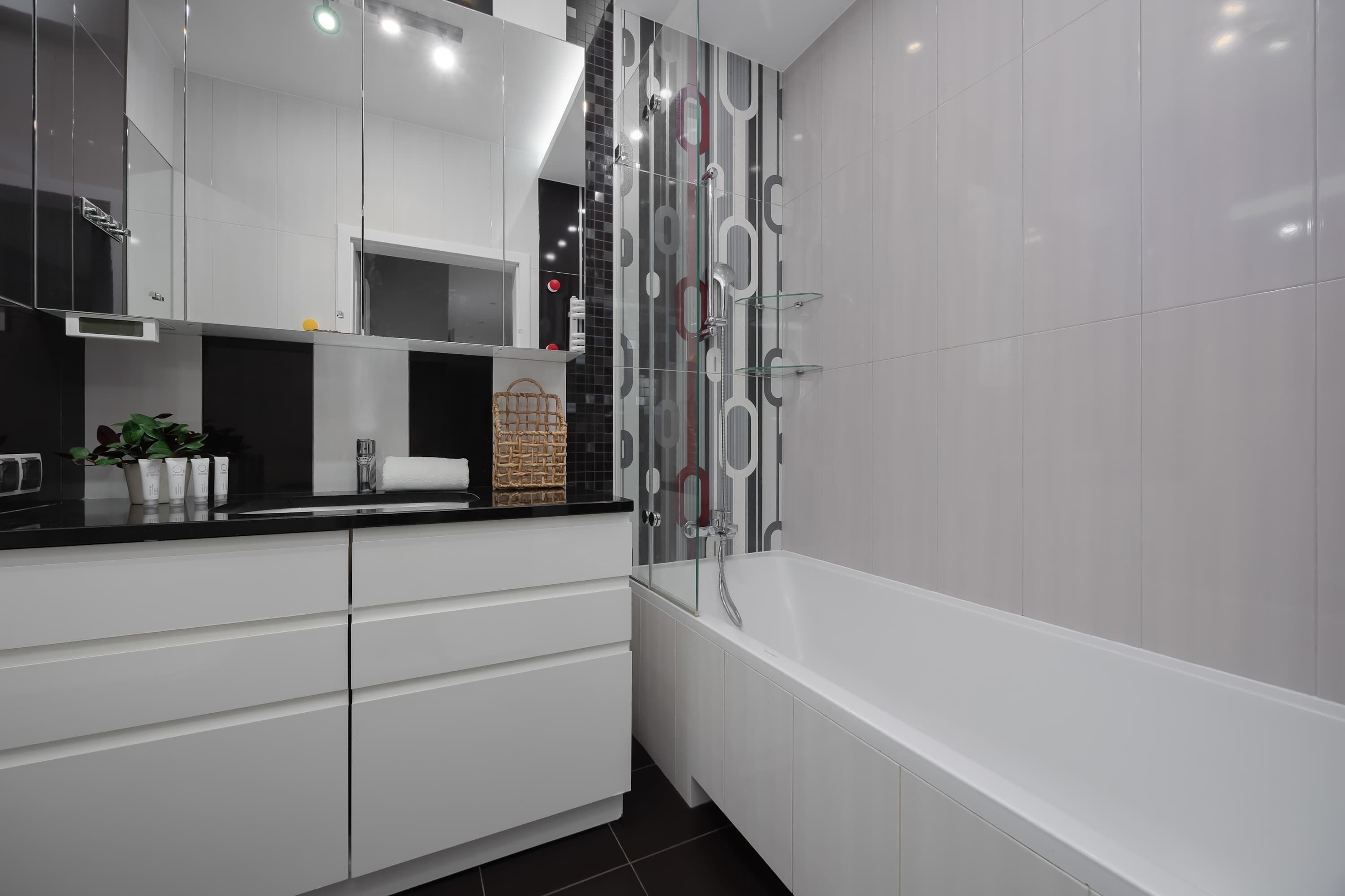 A modern bathroom with a white vanity, a glass shower enclosure, and a white bathtub.